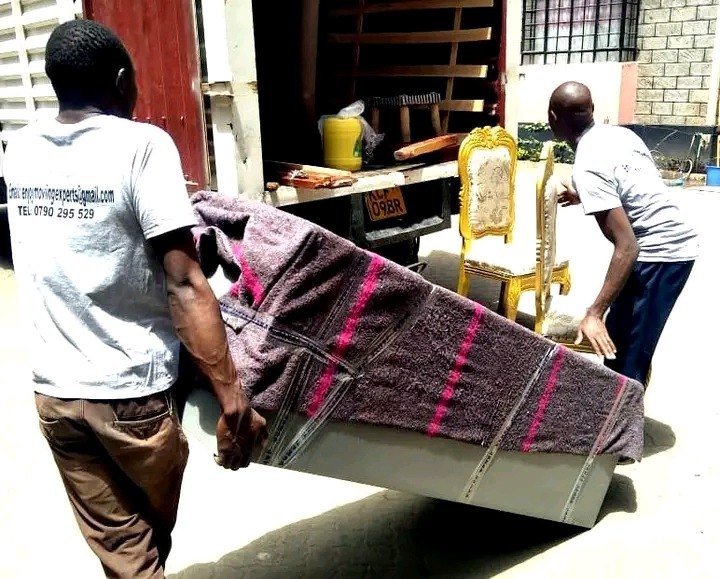 Two movers carrying a wrapped sofa out of a Nairobi home